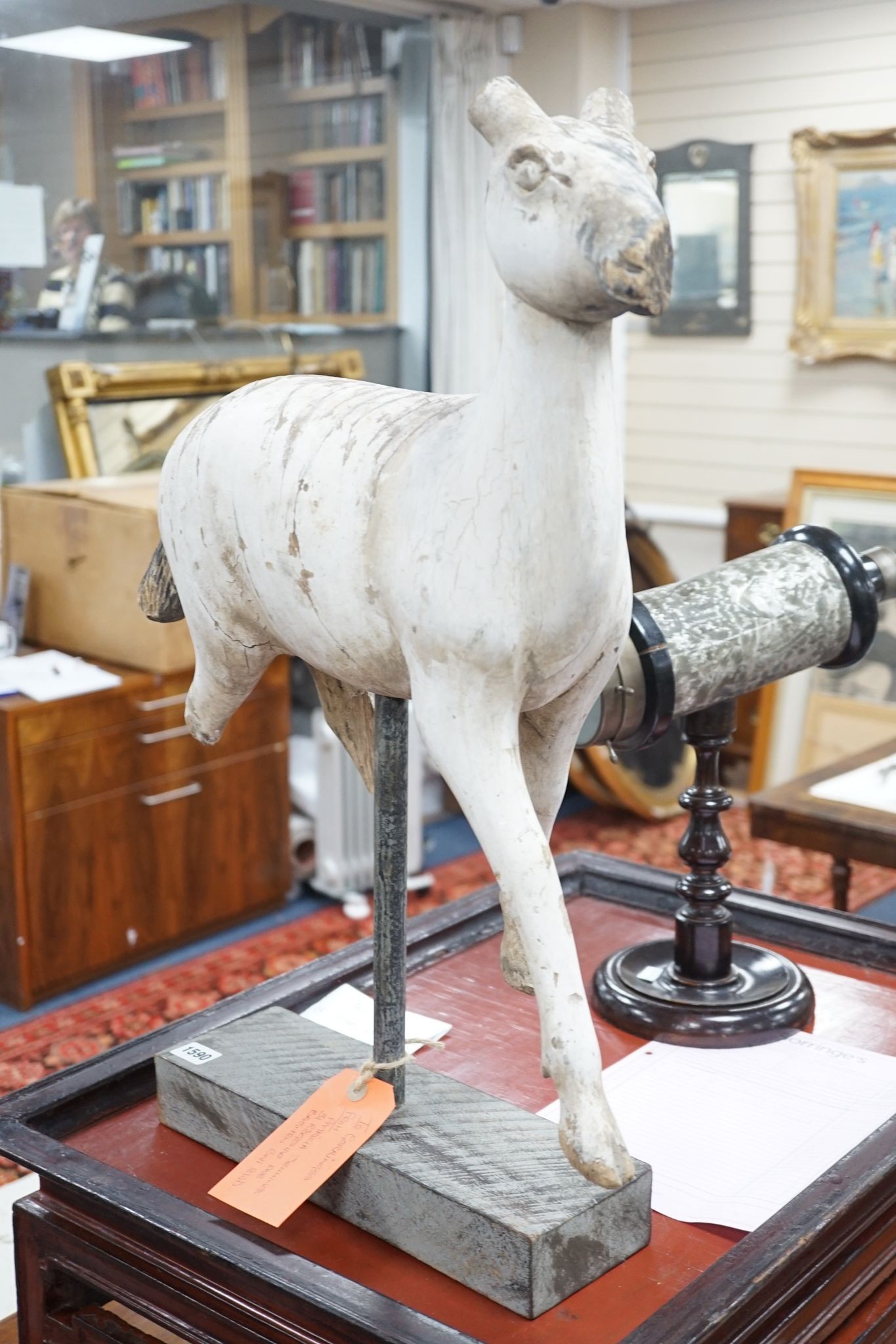 A carved and painted wood model of a goat, with distressed paint, on stand. 66cm